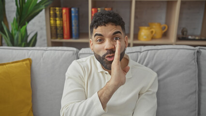 Wall Mural - Hispanic man gesturing silence in a cozy living room with a bookshelf