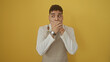 © Krakenimages.com - Shocked young hispanic man with a beard, wearing a white sweater, covers his mouth against a yellow background.