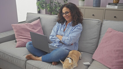 Sticker - Middle-aged hispanic woman smiling while using a laptop on the sofa with her chihuahua in a cozy living room.