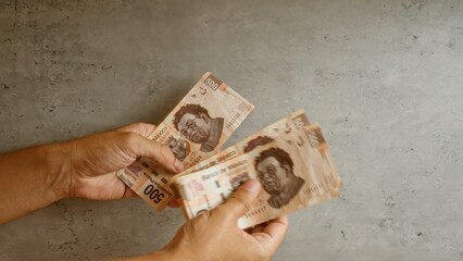 Hands holding mexican pesos against a concrete background, showing 500 peso banknotes.