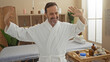 © Krakenimages.com - Smiling man dancing in a spa room while wearing a cozy white robe with wellness decor in the background