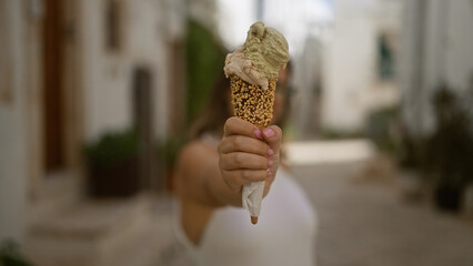 Wall Mural - A young hispanic woman enjoys ice cream on a sunny day while exploring the charming streets of locorotondo, puglia, in italy's historic old town.