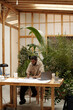 © Clique Images - Architect reviewing blueprints in lush, plant-filled workspace surrounded by greenery