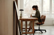 © TrueFrame Collective - Architect sitting at desk in bright minimalist office, focusing on work with laptop and coffee mug