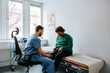 © Maskot - Senior woman showing knee pain to male medical expert while sitting on examination table in doctor's office