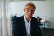 © Maskot - Portrait of smiling senior businessman wearing eyeglasses in office