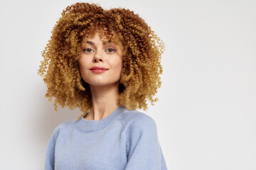 Portrait of a smiling woman with curly hair against a light background, wearing a cozy blue sweater, showcasing natural beauty and confidence in a relaxed setting