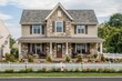 © UMAR SALAM - A traditional two-story home with a peaked roof, classic stone and siding facade, neatly arranged flower beds, and a white picket fence.