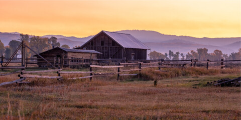 mormon row in grand teton national park. a large, old barn sits in a field with a beautiful sunset i