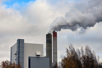 Industrial Emissions. A factory building with a prominent chimney releasing steam into the sky. The balance between industrial production and environmental impact, growth and sustainability.