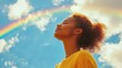 © alauli - Woman with eyes closed under rainbow in blue sky with white clouds. Conceptual image of hope, optimism, happiness, and freedom.
