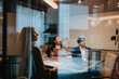 © Maskot - Businessman and businesswomen at desk in board room seen through glass wall