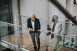 © Maskot - Smiling businessmen discussing while standing by glass railing