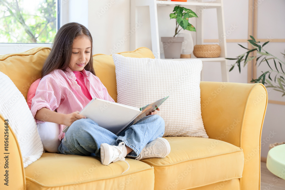 Cute little girl reading book on sofa at home