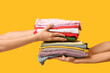 © Pixel-Shot - Female hands with stacks of different clothes on yellow background