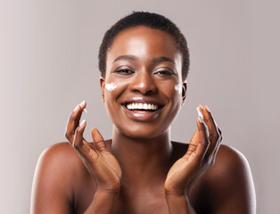 Wall Mural - Skin Care Concept. Closeup Portrait Of Joyful African American Woman Applying Hydration Cream On Face, Grey Studio Background