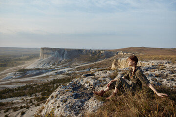 Wall Mural - Woman sitting on cliff edge admiring majestic valley view with mountains in the background for travel and adventure inspiration