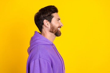 Side profile of positive man with stylish bristle dressed purple hoodie look at sale empty space isolated on yellow color background