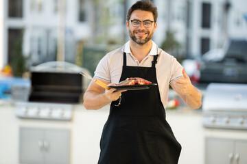 hispanic man cooking a barbeque on a grill, wearing an apron. male roasted steak meat on the gas grill on barbecue grill outdoor in the backyard, summer family picnic, food on the nature.