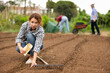 © JackF - Portrait of positive peasant girl while working in garden and planting seeds of fruit plants. Farmers assistant pours plant seeds from bag into soil