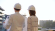 © volha_r - Man and woman architects constructor engineers wearing safety glasses and hardhats, are examining blueprints at a construction site during a sunset, back view. Architecture concept