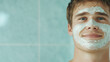 © Tossakan Photos - A young man applying a creamy face mask with his hands, looking into the mirror.