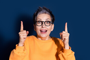 Photo portrait of pretty senior female point up excited empty space wear trendy yellow outfit isolated on dark blue color background