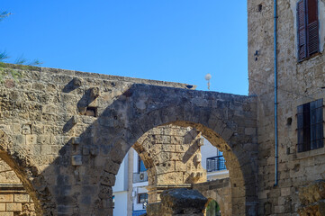 Exploring ancient stone arches beneath a clear blue sky in a historic coastal town