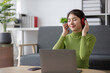 © wichayada - Young Woman Relaxing Happily in the Living Room with Headphones and Laptop, Enjoying Music and Leisure Time