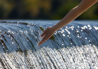 Wall Mural - A hand is reaching into a waterfall, creating ripples in the water