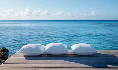 A wooden pier with three white pillows on it, overlooking the ocean