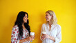 © Pawsitive Vibes - Lady with long black hair in a floral blouse and American female friend with short blonde hair in a white shirt both holding take away coffee cups laughing while standing