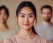 © niti - Asian woman in focus, teammates blurred, beige background, leadership within a team