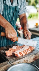 A chef chopping fresh salmon on a wooden cutting board outdoors.