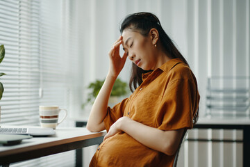 Pregnant woman resting with eyes closed, sitting by window. She is wearing a brown shirt, surrounded by calming home environment with soft light filtering in