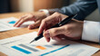© FreemiumStock - Close-up of hands holding a pen over financial documents, highlighting charts for business analysis