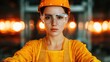 © narak0rn - A focused woman in safety gear, orange helmet and glasses, stands confidently in an industrial setting.