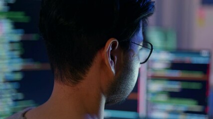 Wall Mural - close-up of a focused male programmer reviewing complex code on a computer monitor in a dimly lit ro