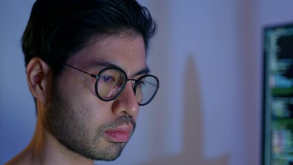 Wall Mural - close-up of a focused male programmer reviewing complex code on a computer monitor in a dimly lit ro