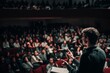 © Vitalii Shkurko - A young speaker passionately gestures while addressing an engaged audience in a large auditorium filled with listeners. The atmosphere is lively and focused