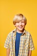 © Seventyfour - Vertical portrait shot of cute little boy wearing casual plaid shirt smiling happily at camera while standing against yellow background in studio, copy space