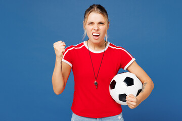 Young sad angry dissatisfied woman fan wear basic red t-shirt cheer up support football sport team hold in hand soccer ball watch tv live stream whistle clench fist isolated on plain blue background.