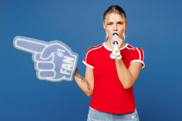 Young happy woman fan wear basic red t-shirt foam 1 fan glove finger up blow pipe cheer up support football sport team hold in hand soccer ball watch tv live stream isolated on plain blue background.