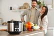 © Pixel-Shot - Multi cooker on table against couple in kitchen, closeup