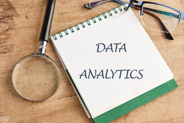 The concept of technology and development. Phrase, words, text DATA ANALYTICS in a notebook on an old background, in a composition with a magnifying glass and glasses