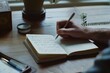 © Victor Bertrand - A hand gracefully writes in a journal on a wooden table by a window, with plants adding a touch of nature to the scene.