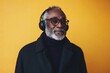 © Nataliia_Trushchenko - Man wearing glasses and headphones is sitting on a yellow background. He is wearing a black coat and a black sweater