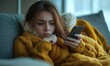 © Onchira - Unhealthy woman suffering from a cold or flu lies on the sofa at home, using phone to browse the internet. Battles disease, virus and fever, feeling unwell and fatigued while seeking online support