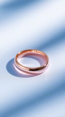 A minimalist rose gold ring is elegantly photographed against a soft blue background, highlighting its smooth surface and shine, Perfect for jewelry marketing, blogs, or lifestyle imagery,