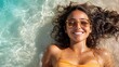 © Lens Legacy - A woman with sunglasses floats in the clear surf, smiling broadly under the sunlight, embodying a moment of relaxation, summer enjoyment, and carefree delight.